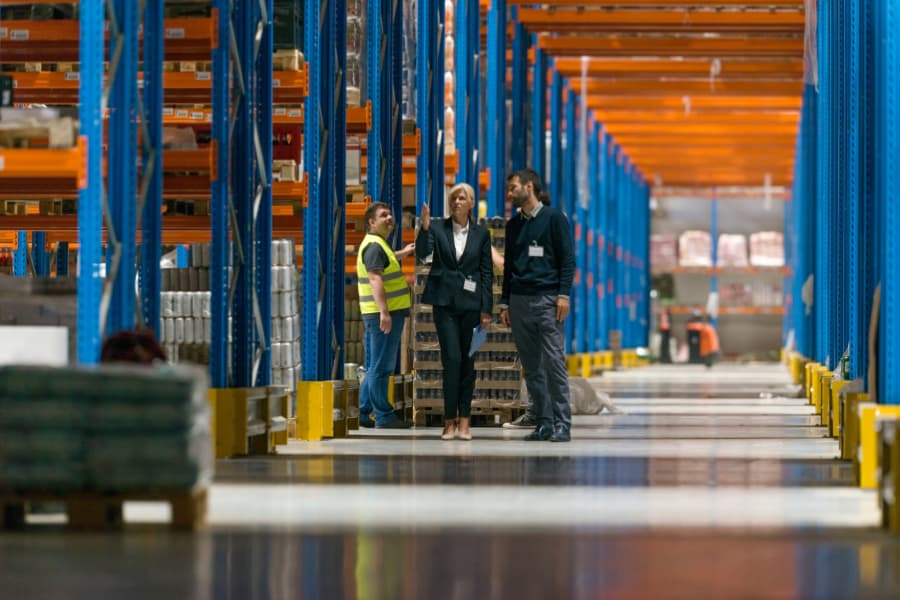 Two businesspeople discuss third-party and fourth-party logistics services with a worker inside a warehouse