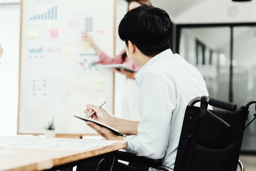 Ryder employee using a wheelchair working at a whiteboard in an office Ryder employee using a wheelchair working at a whiteboard in an office