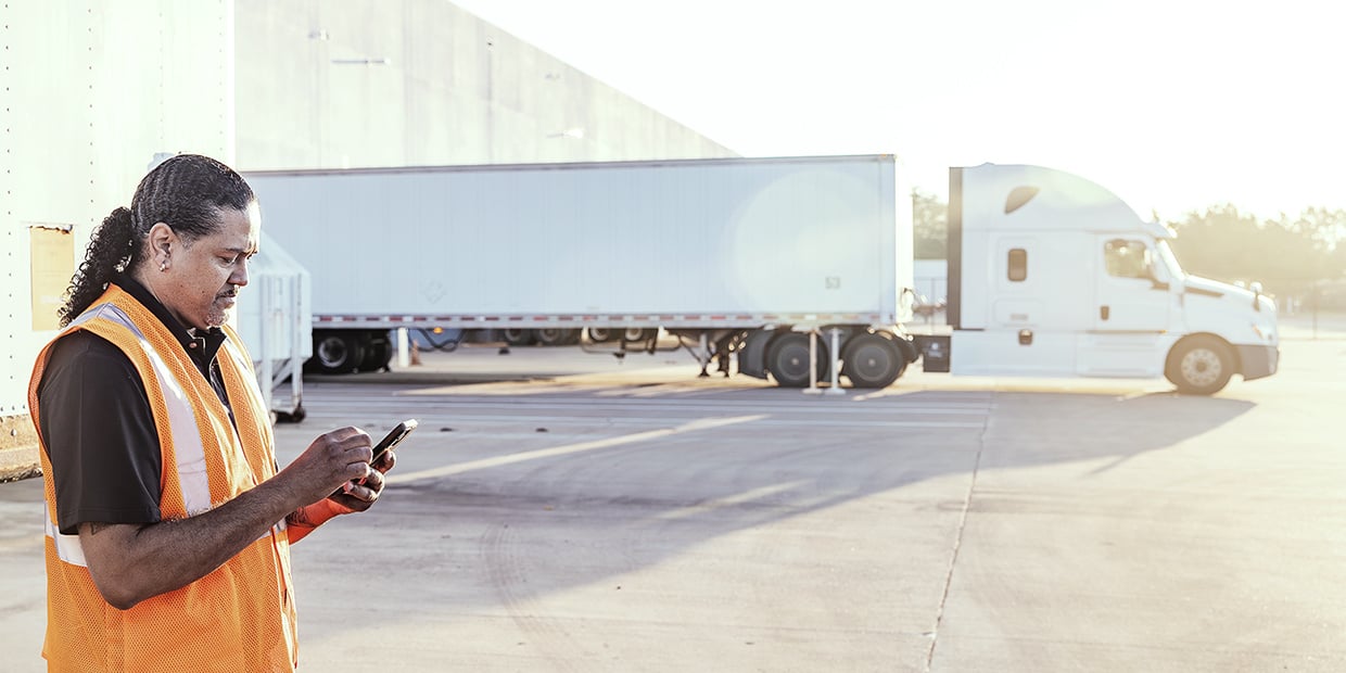 Truck driver using a mobile device near a semi-truck at a loading facility Truck driver using a mobile device near a semi-truck at a loading facility