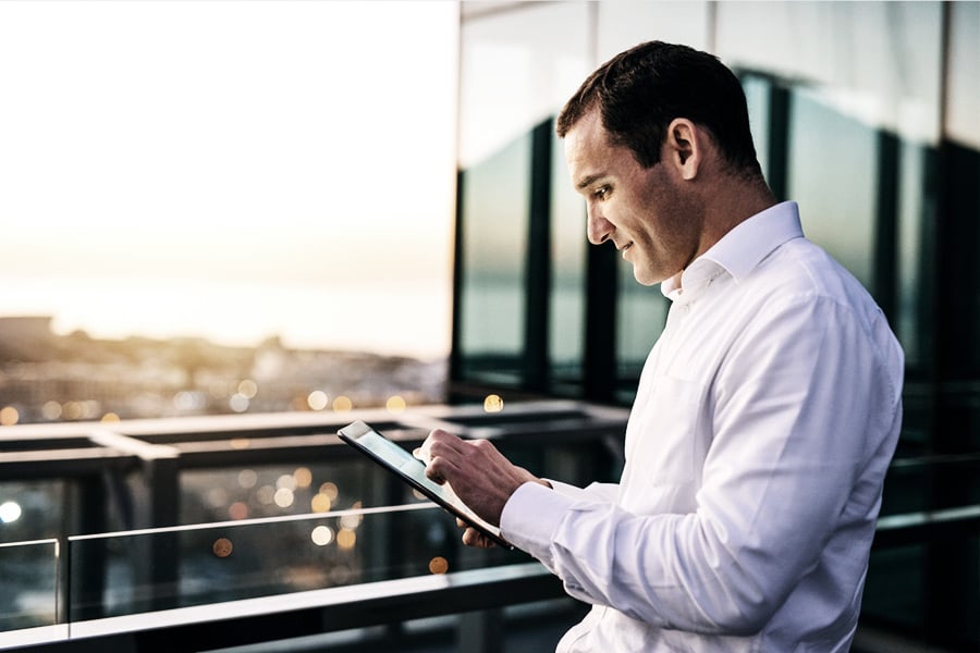 businessman on tablet standing outside on office deck browsing freight brokerage system